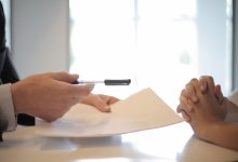 Deux personnes assises face-à-face à bureau signent un contrat.