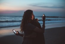 deux personnes sur la plage se serrant dans les bras en regardant leurs téléphones