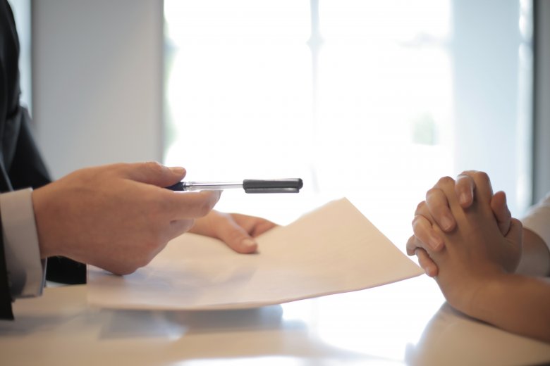 Deux personnes assises face-à-face à bureau signent un contrat.