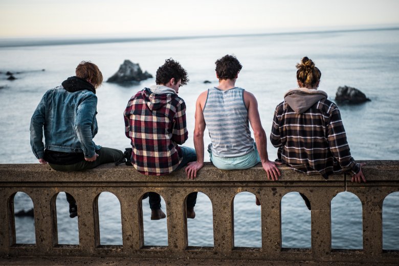 4 jeunes assis sur un garde-fou en bord de mer 